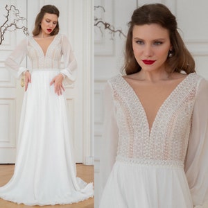 May include: A white wedding dress with long sleeves and a plunging V-neckline. The bodice features delicate lace detailing and a beaded trim. The skirt is flowing and made of a lightweight fabric.