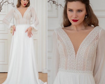 May include: A white wedding dress with long sleeves and a plunging V-neckline. The bodice features delicate lace detailing and a beaded trim. The skirt is flowing and made of a lightweight fabric.
