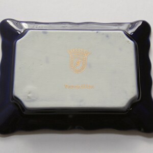 May include: A rectangular, ceramic tray with a wavy, dark blue border. The center is white with a gold emblem and the word "Versailles" in gold lettering. The tray is likely for decorative use.