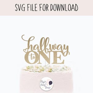 May include: Gold glitter cake topper with the text "halfway to one" in a cursive font. The topper is on top of a white cake with a pink frosting.