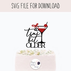 May include: Black cake topper with the text "a tiny bit OLDER" and a martini glass design with a red bow and cherry. The words "SVG FILE FOR DOWNLOAD" are at the top. The cake topper is on top of a white cake.
