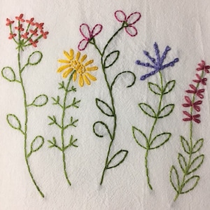 Puede incluir: Dise&ntilde;o floral bordado con cinco tipos diferentes de flores en tonos rojos, amarillos, morados y rosas. Las flores tienen tallos y hojas verdes, bordadas sobre un fondo de tela blanca.