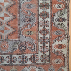 May include: A close-up of a rug with a geometric pattern in shades of orange, brown, and white. The rug has a fringe border.