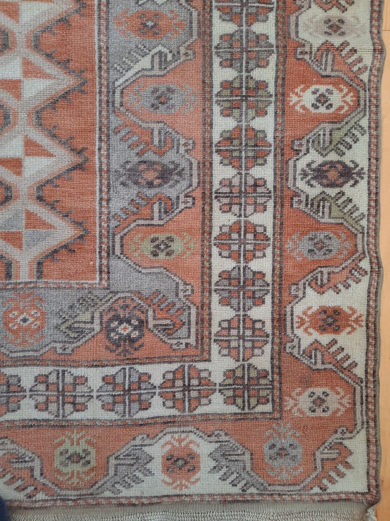 May include: A close-up of a rug with a geometric pattern in shades of orange, brown, and white. The rug has a fringe border.