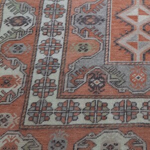 May include: Close-up of a vintage rug with a faded orange and cream color scheme. The rug features intricate geometric patterns and floral motifs.