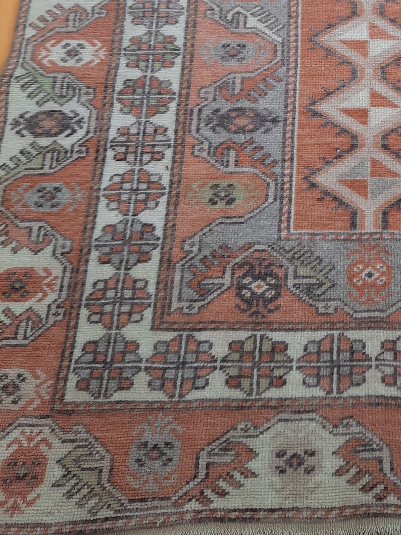 May include: Close-up of a vintage rug with a faded orange and cream color scheme. The rug features intricate geometric patterns and floral motifs.