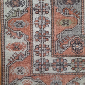 May include: Close-up of a vintage rug with a geometric pattern in shades of beige, brown, and orange. The rug has a worn, distressed look, adding to its character.