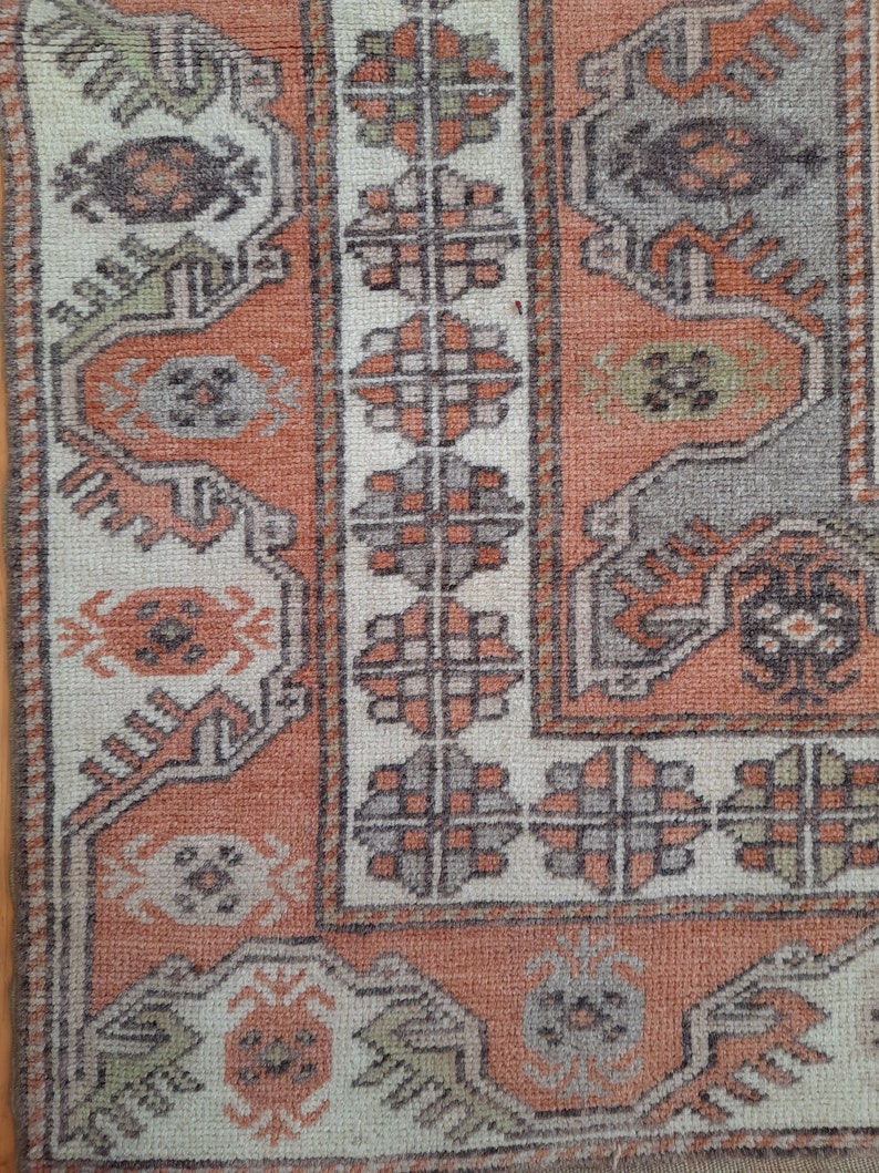 May include: Close-up of a vintage rug with a geometric pattern in shades of beige, brown, and orange. The rug has a worn, distressed look, adding to its character.
