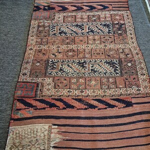 Puede incluir: Una alfombra rectangular con una mezcla de diseños geométricos y a rayas. La alfombra presenta una paleta de colores marrón, negro y beige. El diseño incluye formas geométricas repetidas y rayas horizontales, creando una apariencia texturizada.