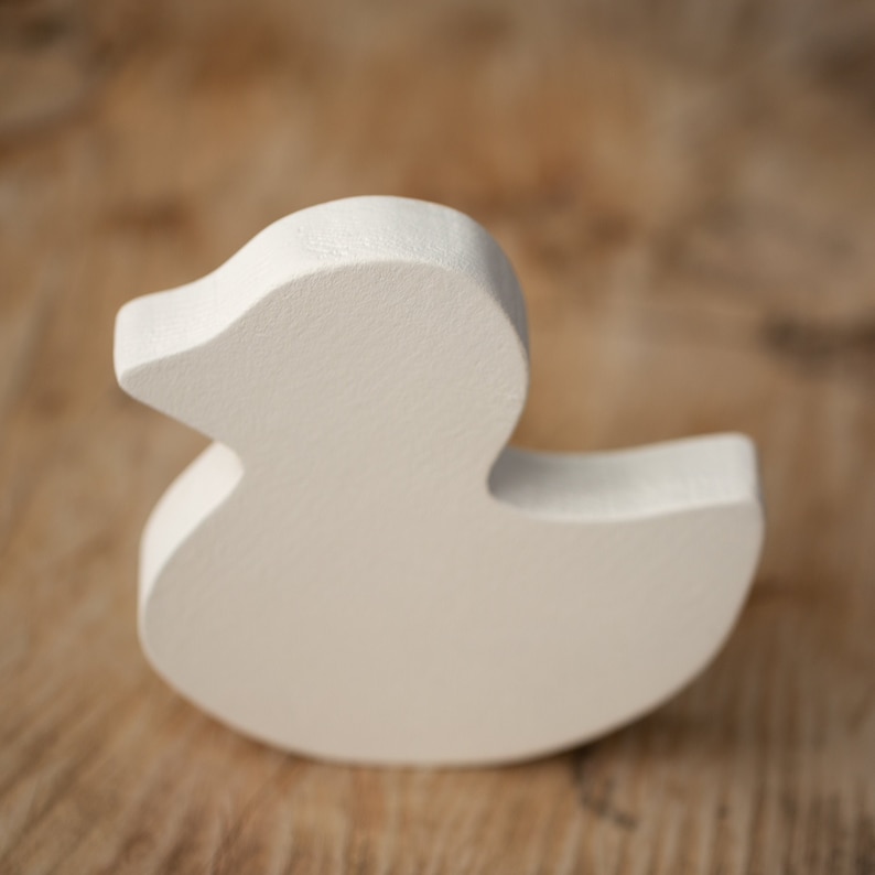 May include: A solid, off-white wooden duck figurine. The duck has a smooth, rounded body and a detailed beak. The figurine is a simple, yet charming decorative item, perfect for a nursery or home decor.
