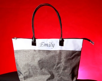Peut inclure: Un sac fourre-tout gris et blanc avec des anses noires. Le sac porte le nom "Emily" brodé sur le devant.