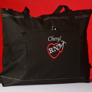 Peut inclure: Sac fourre-tout noir avec un c&oelig;ur rouge et les lettres "RN" brod&eacute;es dessus. Le nom "Cheryl" est brod&eacute; au-dessus du c&oelig;ur. Le sac a une poche en filet sur le c&ocirc;t&eacute;.