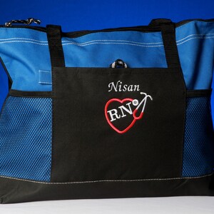 Peut inclure: Sac fourre-tout bleu et noir avec une poche en filet. Le sac est personnalis&eacute; avec un motif brod&eacute; avec le nom "Nisan" et un c&oelig;ur rouge avec les lettres "RN" et un st&eacute;thoscope.