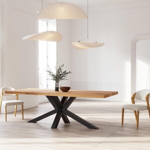 May include: A wooden dining table with a black metal base featuring a starburst design. The table is set in a modern dining room with white walls and three white pendant lights.