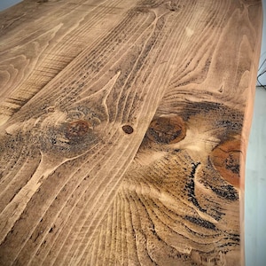 May include: Close-up of a rustic wooden table top with a natural wood grain pattern and dark brown knots. The wood has a warm, honey-colored stain.