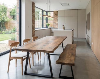 Puede incluir: Una mesa de comedor de madera con borde natural, veteado visible y patas de metal negro, acompañada de dos sillas de madera con asientos tapizados en blanco y un banco de madera a juego con patas de metal negro en una cocina.