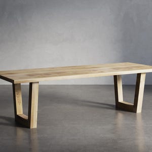 Könnte beinhalten: Ein Esstisch aus hellem Holz mit einer rechteckigen Tischplatte und einem schlichten, modernen Design. Der Tisch hat vier Beine, die U-förmig sind.