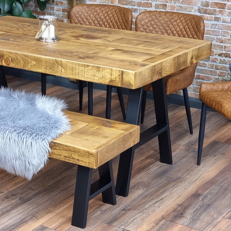 May include: A rustic wooden dining table with black metal legs and a matching bench. The table has a distressed finish and is made of reclaimed wood. The bench has a gray faux fur throw on top.