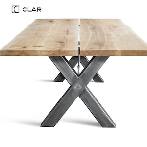May include: A wooden table with a live edge top and two sets of metal X-shaped legs. The table is made of natural wood with a light brown finish. The legs are made of steel with a dark gray finish.