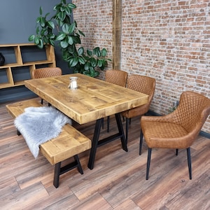 May include: A rustic wooden dining table with a distressed finish and black metal legs. The table is surrounded by four chairs with brown leather upholstery. The chairs have a quilted design and black metal legs. The table is set with a glass candle holder.