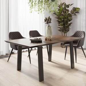 Könnte beinhalten: Ein dunkelbrauner Esstisch mit schwarzen Metallbeinen. Der Tisch ist mit vier Stühlen gedeckt, von denen zwei auf dem Bild zu sehen sind. Die Stühle sind mit braunem Leder bezogen und haben ein gestepptes Design. Der Tisch ist mit einem Buch und einer Blumenvase gedeckt.