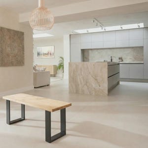May include: A wooden bench with black metal legs in a modern living space. The bench is in the foreground, with a kitchen island and cabinets in the background. A decorative light fitting hangs from the ceiling.