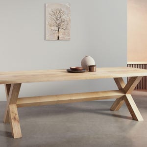 May include: A light wood dining table with a rectangular top and a single shelf. The table has an X-shaped base.