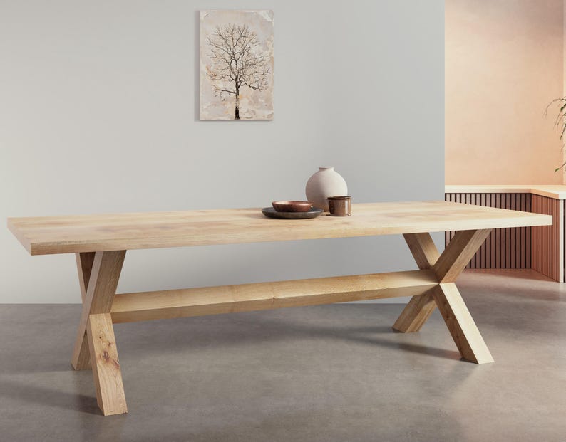 May include: A light wood dining table with a rectangular top and a single shelf. The table has an X-shaped base.