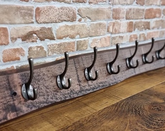 Puede incluir: Un perchero de madera rústico con un acabado desgastado y ocho ganchos de metal. El perchero está montado en una pared con un fondo de ladrillo.