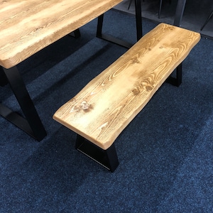 May include: A wooden bench with a natural wood finish and black metal legs. The bench is made of reclaimed wood and has a rustic look.