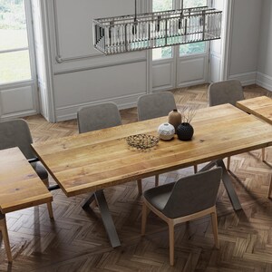 Könnte beinhalten: Ein Esstisch aus Holz mit einem Metallgestell und sechs Stühlen. Der Tisch hat eine natürliche Holzoptik und ist mit zwei Blättern erweiterbar. Die Stühle sind mit einem grauen Stoff bezogen.