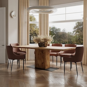 Op de afbeelding: Een houten eettafel met een rustieke afwerking en een zwarte metalen basis. Zes bruine gestoffeerde stoelen met zwarte metalen poten staan rond de tafel. De tafel staat in een kamer met grote ramen en beige gordijnen.