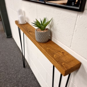 Op de afbeelding: Een rustieke houten consoletafel met zwarte haarspeldpoten. De tafel is versierd met een potplant en twee witte kaarsen.