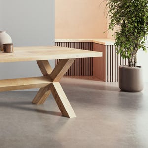 May include: A light wood dining table with a wide, rectangular top and an X-shaped base. The table is in a room with a light gray wall and a light peach wall with a wooden slatted bench.