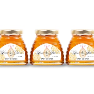 May include: Three small glass jars filled with golden honey, each topped with a gold lid. Each jar has a label that reads "Love is Sweet" with the date "12.30.24" and the name "BABY COOPER".