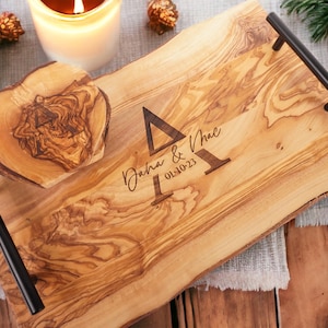 Puede incluir: Una bandeja de servir de madera con un acabado de grano de madera natural y asas de metal negro. La bandeja tiene un recorte en forma de corazón y está grabada con el texto "Dana & Mac 01-10-23".