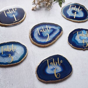 May include: Six agate table numbers with gold foil lettering. The numbers are 1 through 6. The agate is blue and white with a gold rim.