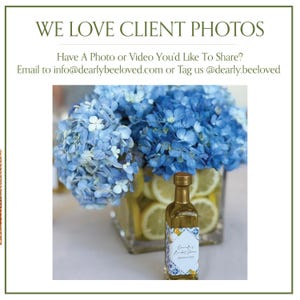 May include: An image featuring a small, gold-topped bottle with a decorative label, likely a favor. The label has a blue and white design with text. A bouquet of blue hydrangeas and lemon slices in a glass vase are in the background. Text reads: "WE LOVE CLIENT PHOTOS".