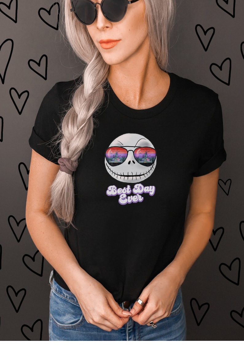 K&ouml;nnte beinhalten: Schwarzes T-Shirt mit einem wei&szlig;en Comic-Gesicht, das eine Sonnenbrille tr&auml;gt. Die Sonnenbrille reflektiert ein farbenfrohes Bild einer Burg. Der Text "Best Day Ever" ist in Lila unter dem Gesicht aufgedruckt.
