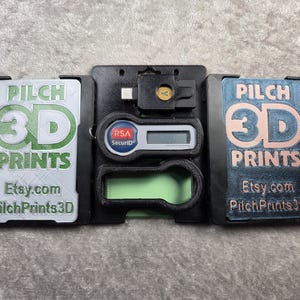 May include: A black 3D-printed case with a central compartment holding a security token and a USB device. Two side panels display "PILCH 3D PRINTS" and "Etsy.com PilchPrints3D" in green and copper-colored text.