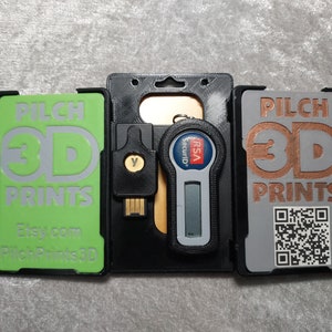 May include: A collection of 3D-printed items, including cardholders and a USB device. The cardholders are in green and gray, with the text "PILCH 3D PRINTS" and a QR code. A black cardholder holds a security token. The Etsy shop name is visible.