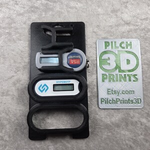Può includere: Supporto nero stampato in 3D con due token di sicurezza digitali e una carta argentata. I token hanno display digitali e il testo "HYPEROTP" e "RSA Secure". La carta presenta "PILCH 3D PRINTS" e l'indirizzo Etsy.com.