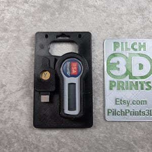 Può includere: Portachiavi di sicurezza nero stampato in 3D con un dispositivo RSA SecurID e un connettore USB-C. Un'etichetta argentata con testo verde recita "PILCH 3D PRINTS" e "Etsy.com PilchPrints3D".