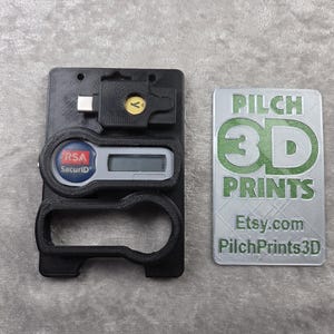 Può includere: Supporto nero stampato in 3D per dispositivi di sicurezza con connettore USB-C, display digitale e logo RSA SecurID. Un'etichetta argentata con testo verde riporta "PILCH 3D PRINTS" e "Etsy.com PilchPrints3D".