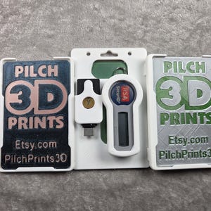 May include: Three white plastic holders with 3D printed items. The holders contain a USB drive, a security token, and two cards with the text "PILCH 3D PRINTS" and Etsy.com address.