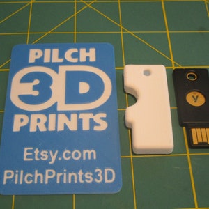 Puede incluir: Una llave en blanco de plástico blanco con un diseño recortado, una llave USB negra con una letra "Y" dorada en ella y una tarjeta azul con el texto "Pilch 3D Prints Etsy.com PilchPrints3D" impreso en ella.