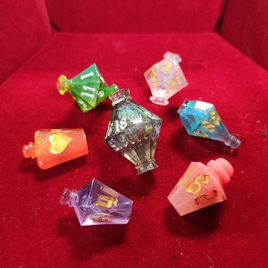 Könnte beinhalten: Sieben bunte, schillernde Glaswürfel mit goldenen Zahlen und Symbolen. Die Würfel befinden sich in einer roten Samtbox.