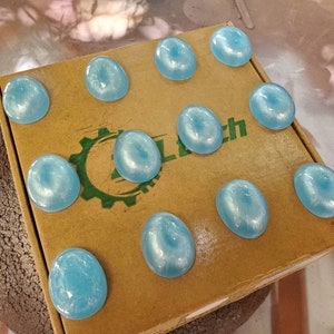 May include: A cardboard box with the word "Clutch" printed on it. The box is filled with 10 light blue round objects.