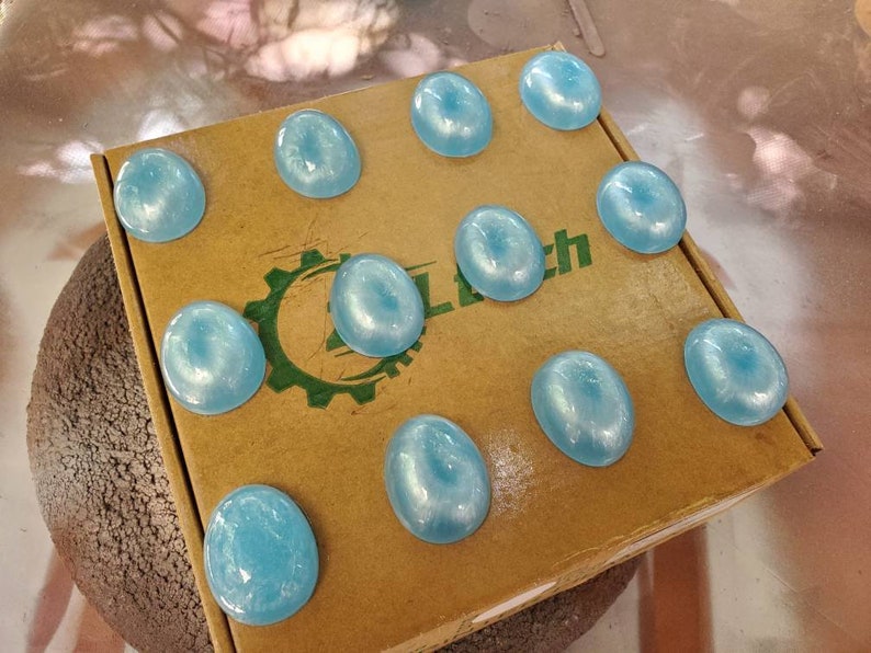 May include: A cardboard box with the word "Clutch" printed on it. The box is filled with 10 light blue round objects.