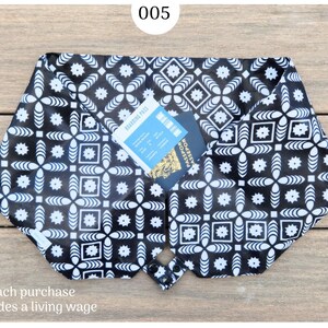 May include: Black and white patterned travel organizer with a boarding pass and passport inside. The organizer has a geometric floral design and is buttoned closed. The text "each purchase provides a living wage" is at the bottom.